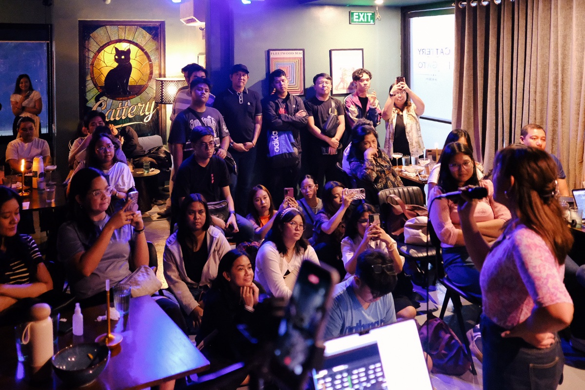 a full house at Cattery — a crowd seated and standing through a live set, phones up, drinks on the tables, the stained-glass cat glowing on the wall behind