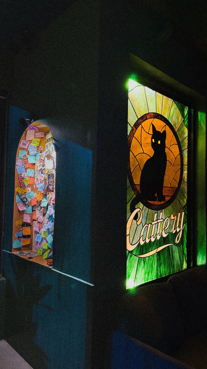 The note-covered alcove beside Cattery's stained-glass black-cat window, glowing amber and green